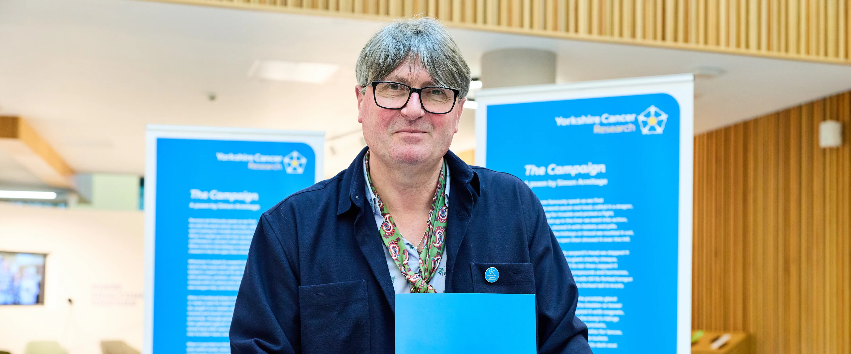 Poet Laureate Simon Armitage stands in front of large printouts of his poem, "The Campaign"