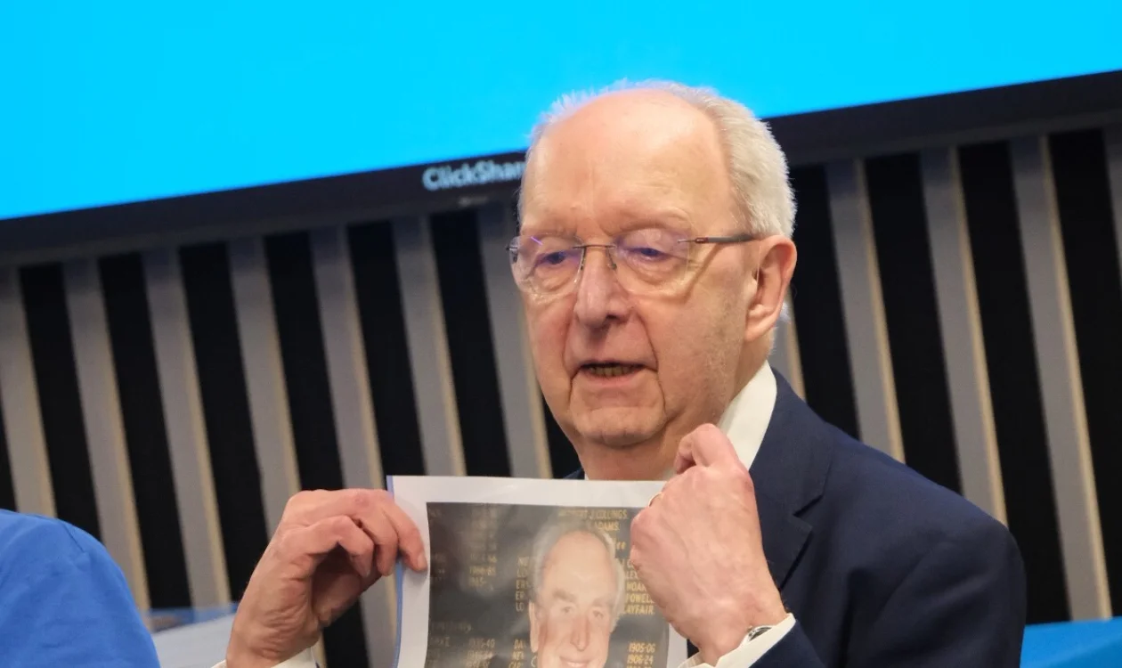A man in a suit and glasses engages in conversation with someone off camera