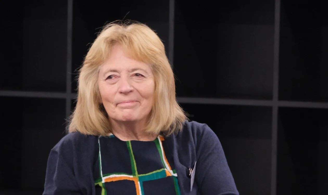 A lady in a long patterned dress sits in a chair in discussion