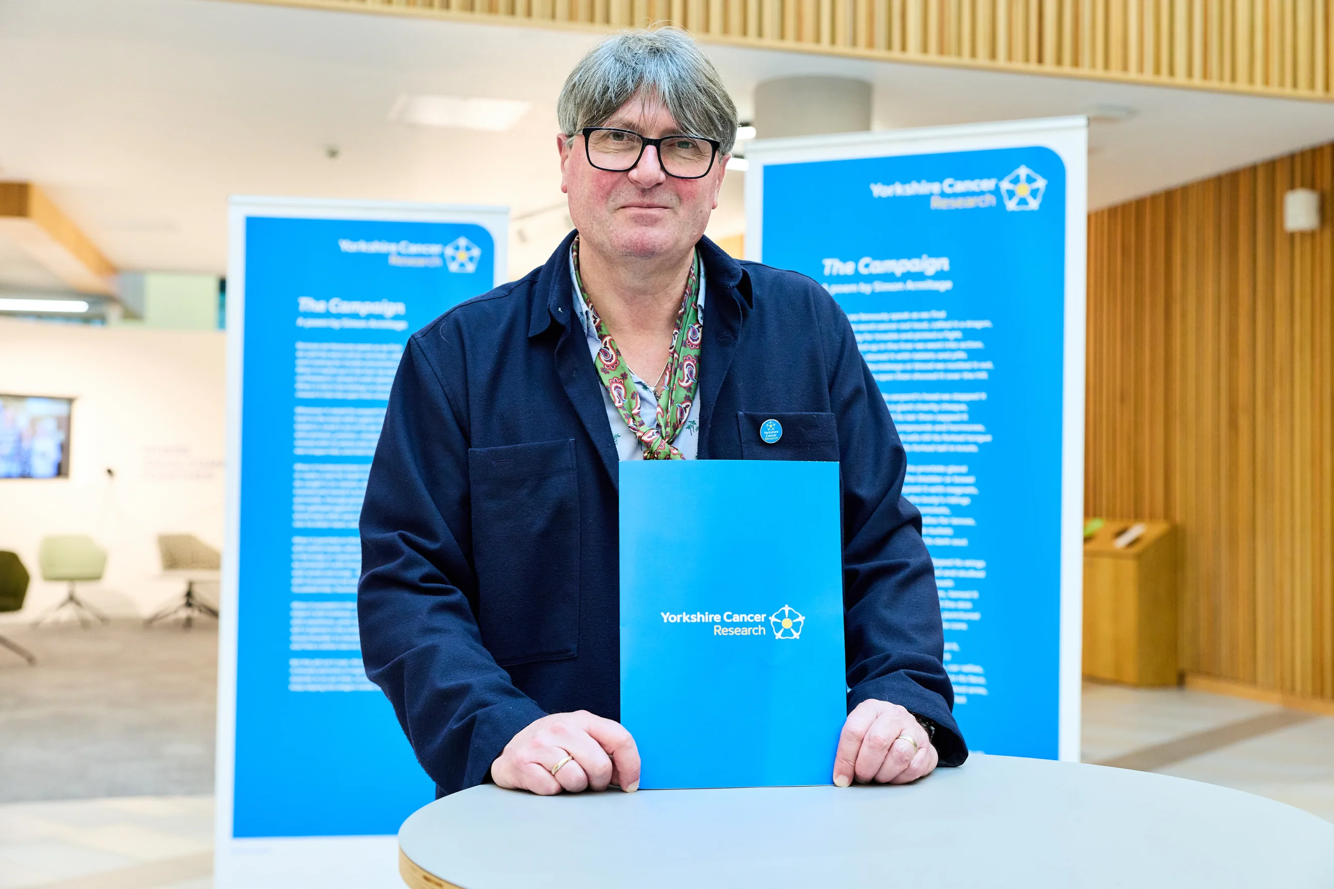 Poet Laureate Simon Armitage stands in front of large printouts of his poem, "The Campaign"