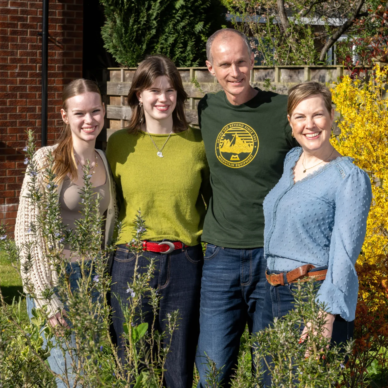 A family stands with arms around each other smiling in a garden