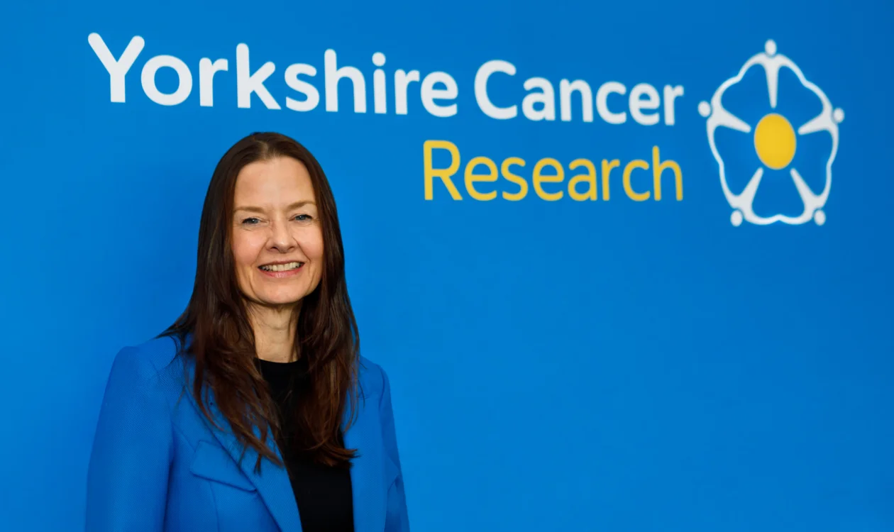 A lady in a blue blazer stands in front of a Yorkshire Cancer Research logo
