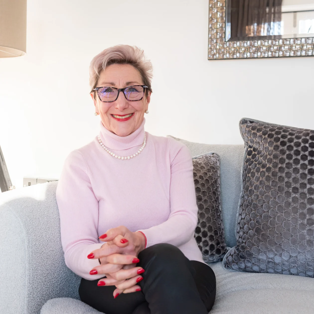 A lady sits on a sofa smiling at the camera