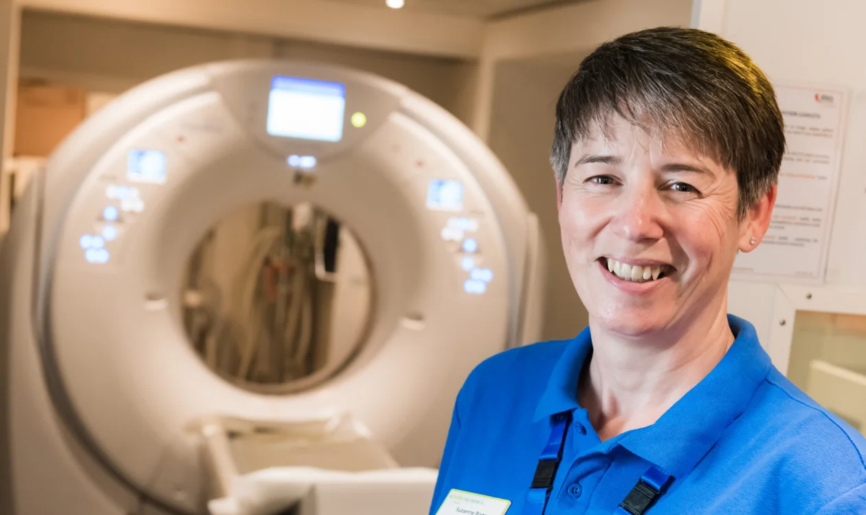 Senior Research Nurse standing in front of a CT scanner on a mobile screening unit