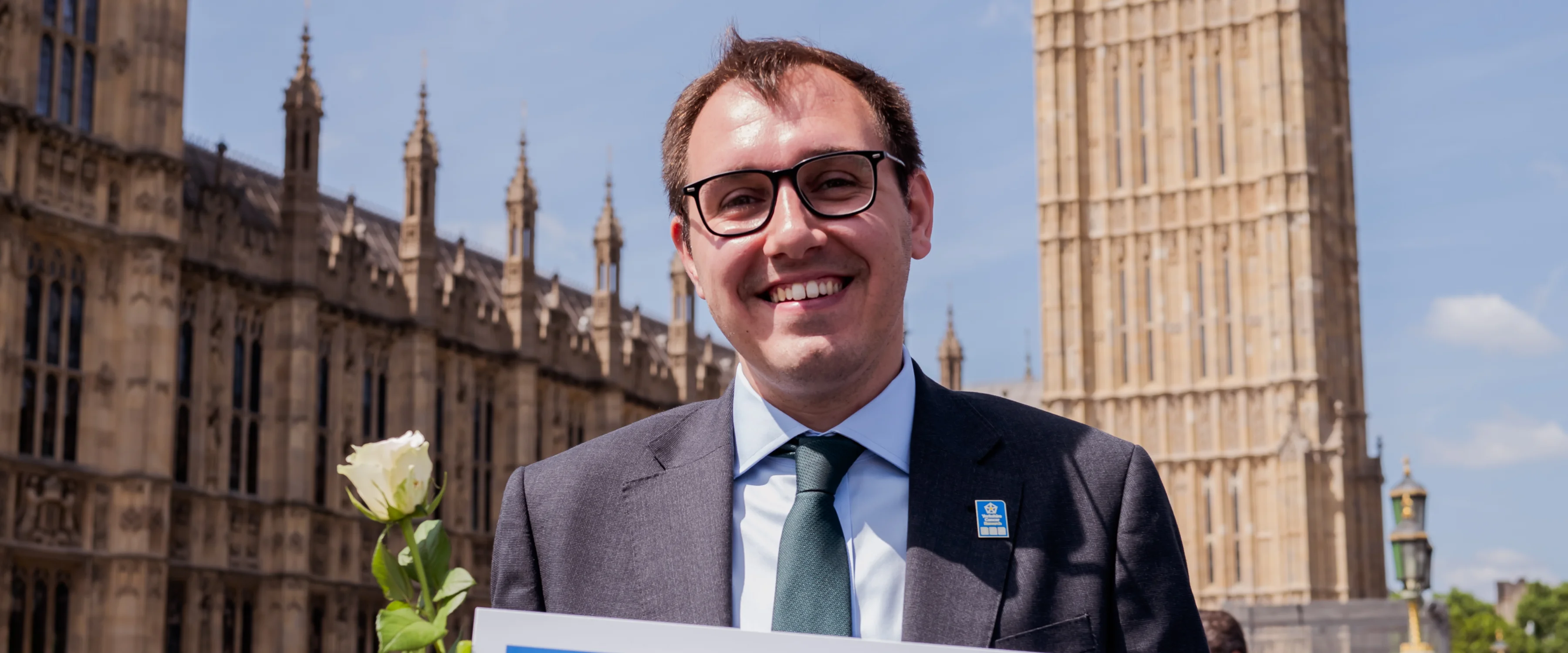 Yorkshire MP standing in front of Houses of Parliament and Big Ben with a placard reading 'I'm standing with Yorkshire for a cancer-free future'.
