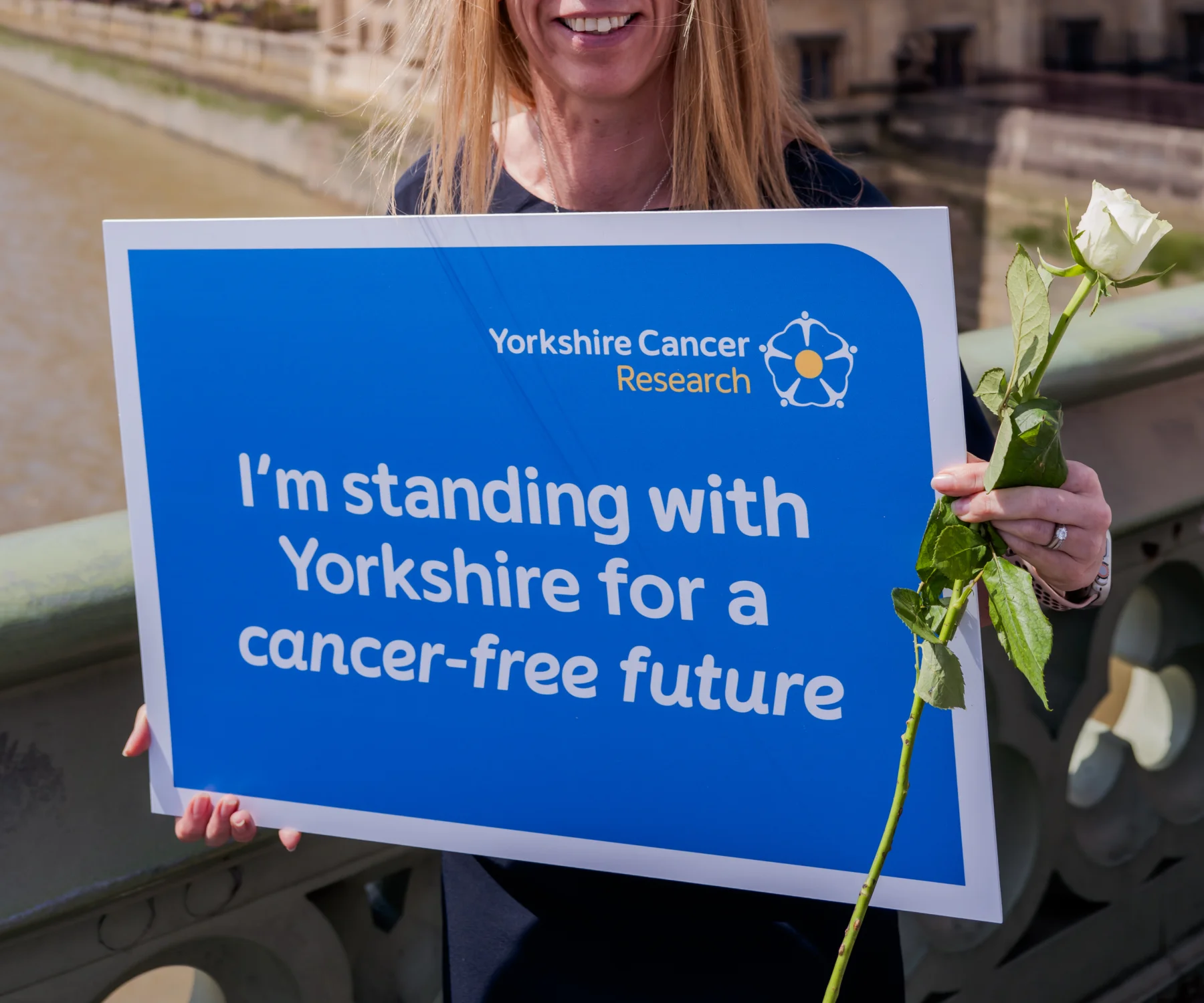 A person standing in-front of the Houses of Parliament with a placard reading 'I'm standing with Yorkshire for a cancer-free future"