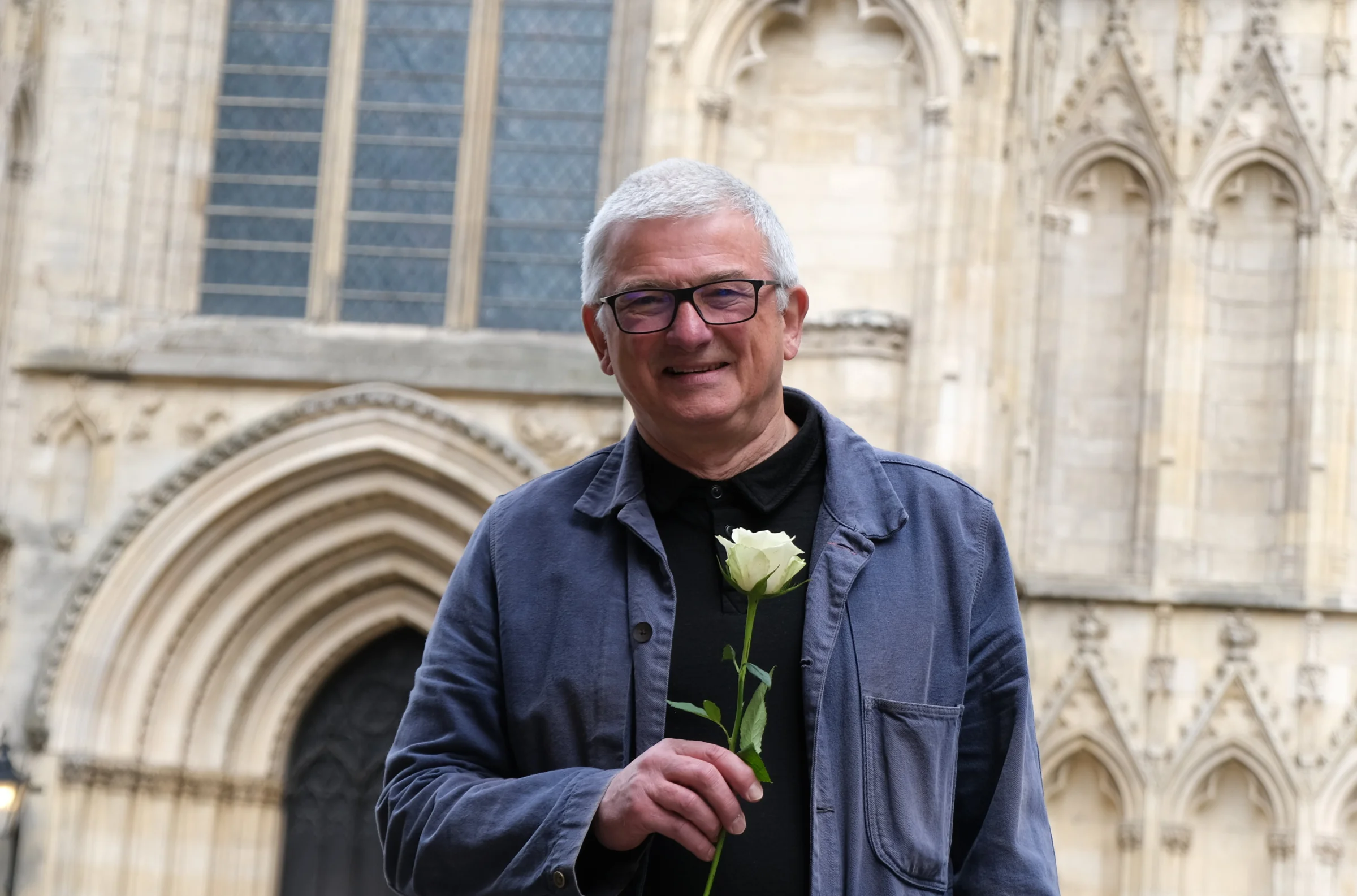 A male holding a white rose, standing in front of York Minster.