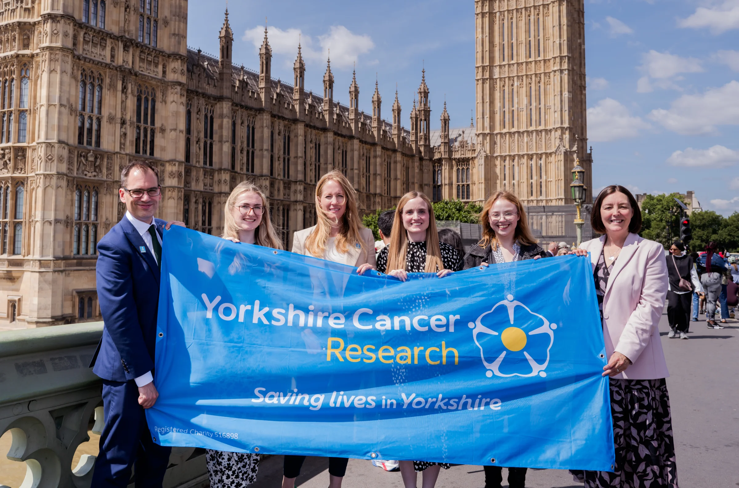 Yorkshire Cancer Research team outside of the Houses of Parliament, holding a Yorkshire Cancer Research flag