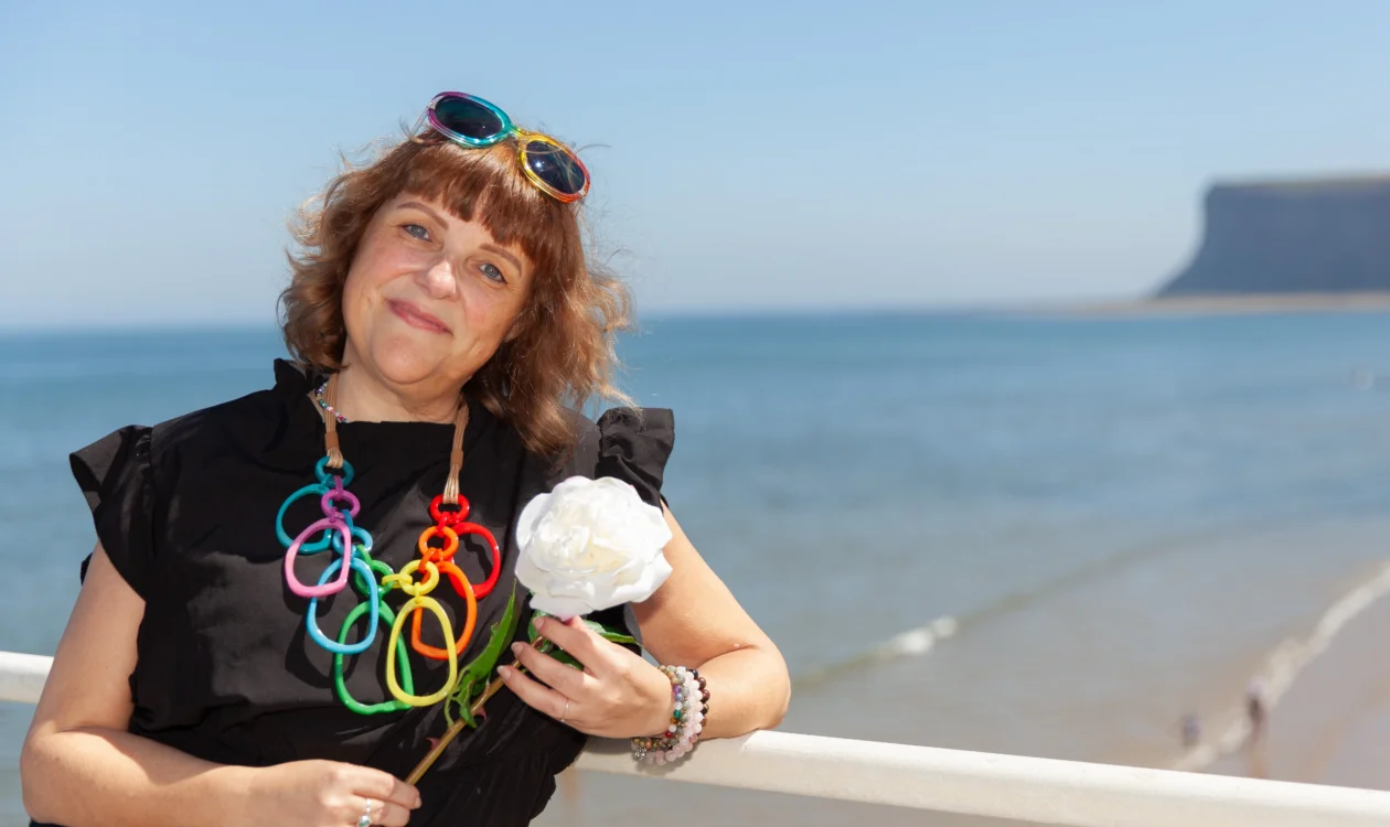 Nicky standing in front of a beach holding a white rose