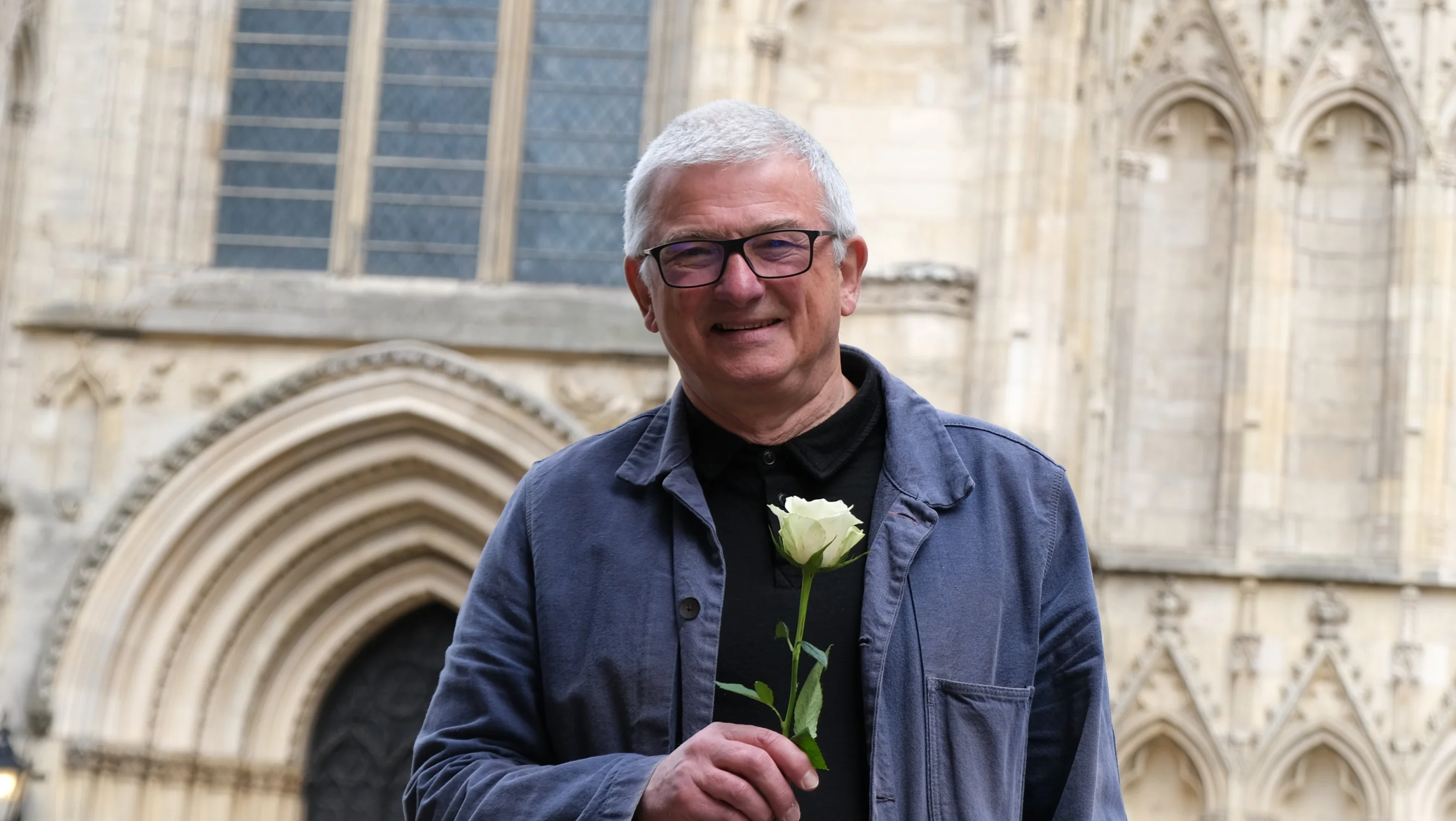 A male holding a white rose, standing in front of York Minster.