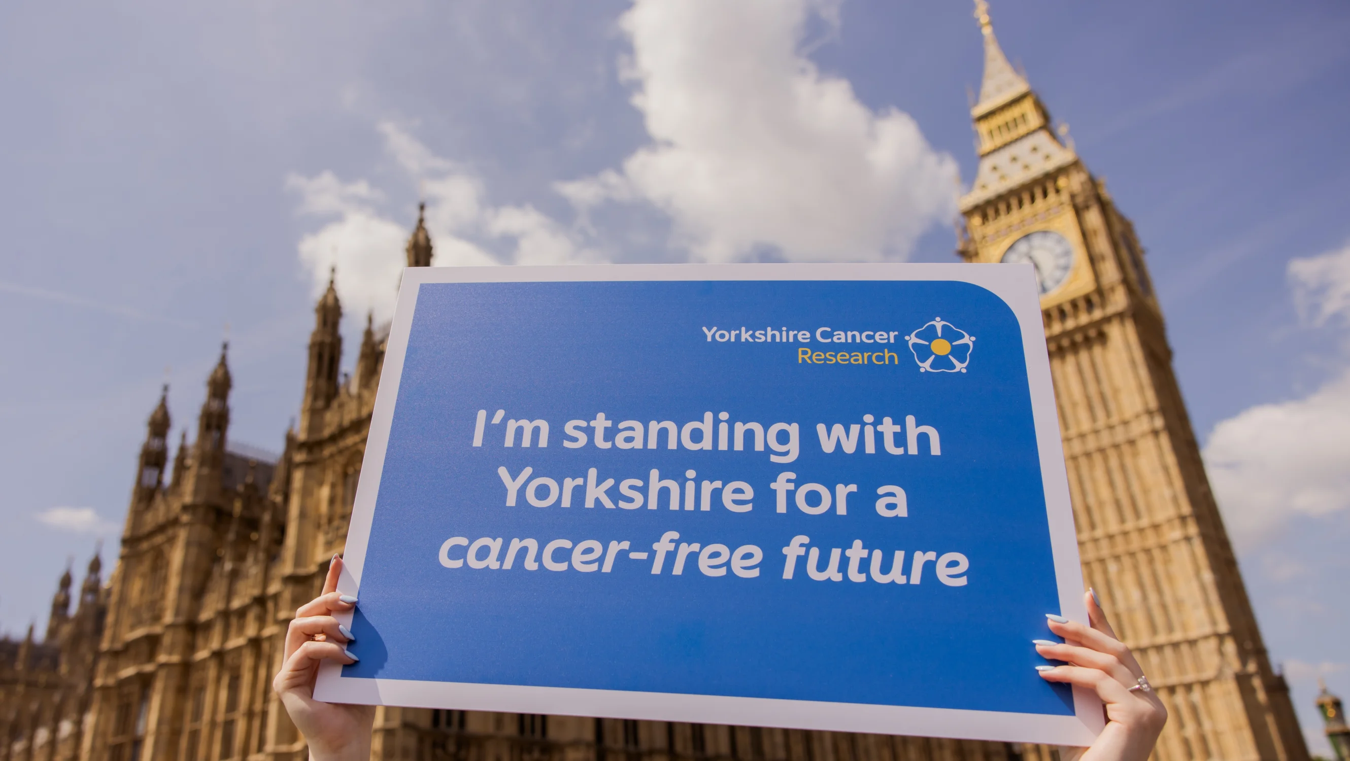 A placard held up infront of the Houses of Parliament reading "I'm standing with Yorkshire for a cancer-free future"