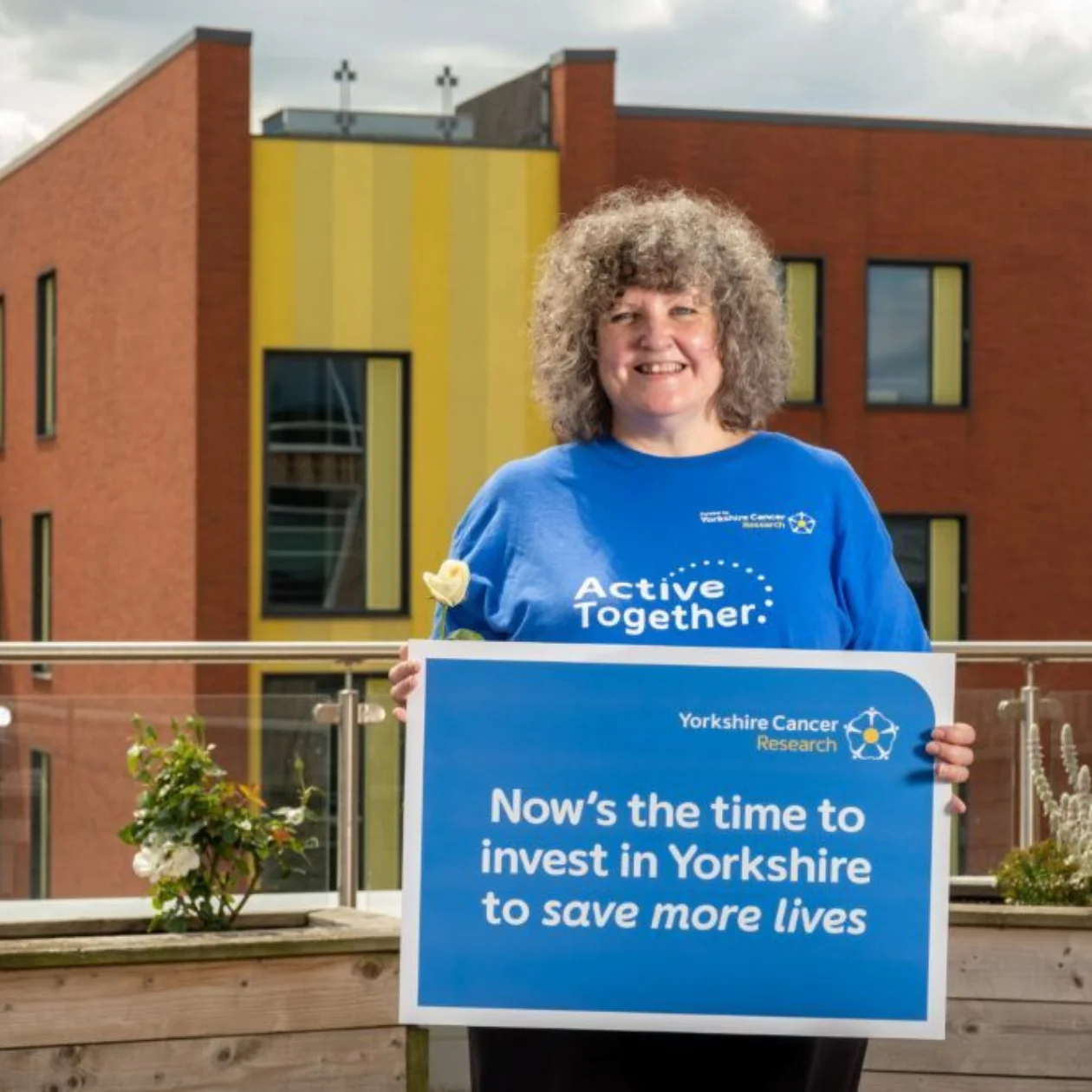 A woman standing outside in the sunshine holding a placard which reads "Now's the time to invest in Yorkshire to save more lives"
