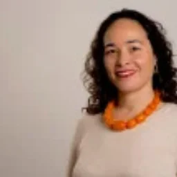 A lady with dark curly hair and a chunky necklace smiling