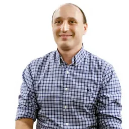 A man in a checked, blue shirt smiles