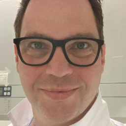 A man with dark hair and glasses smiling