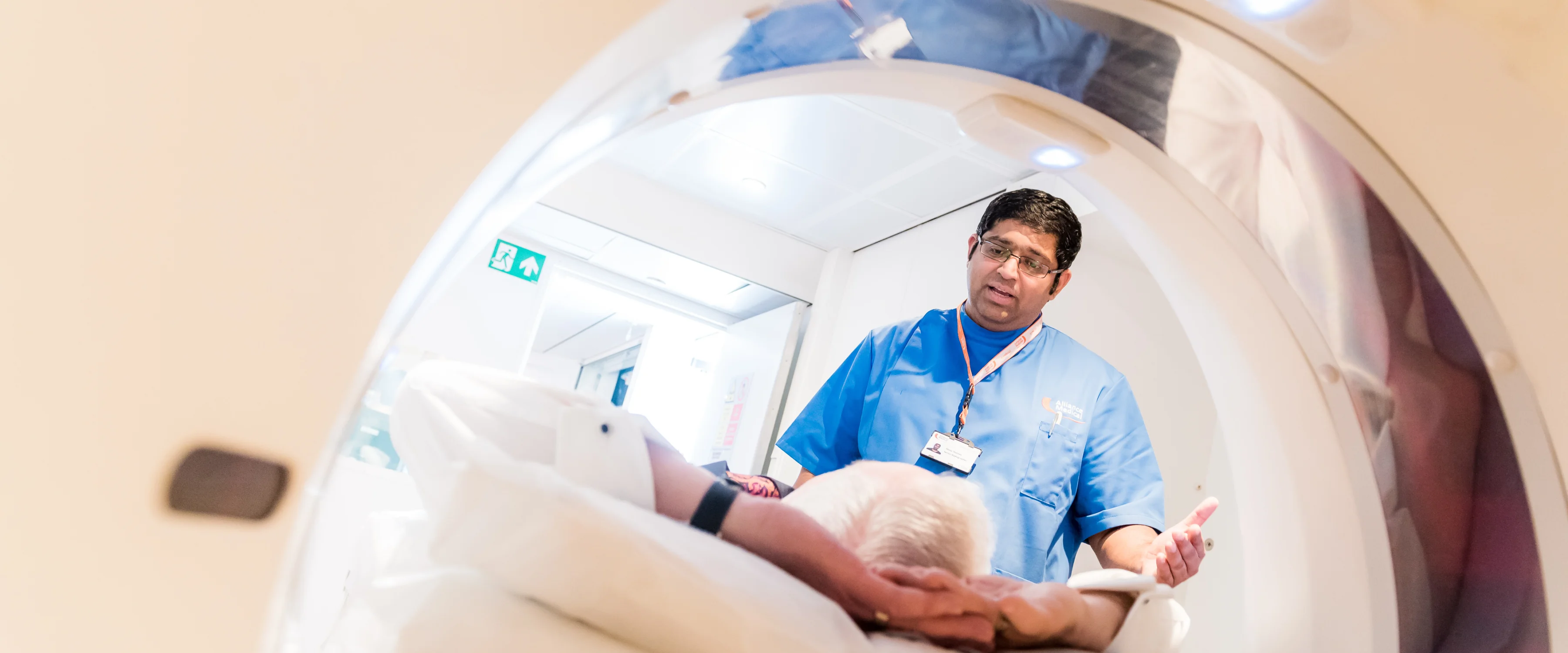 A male clinicia speaking to a patient who is lying on their back, about to be moved into a CT scanner