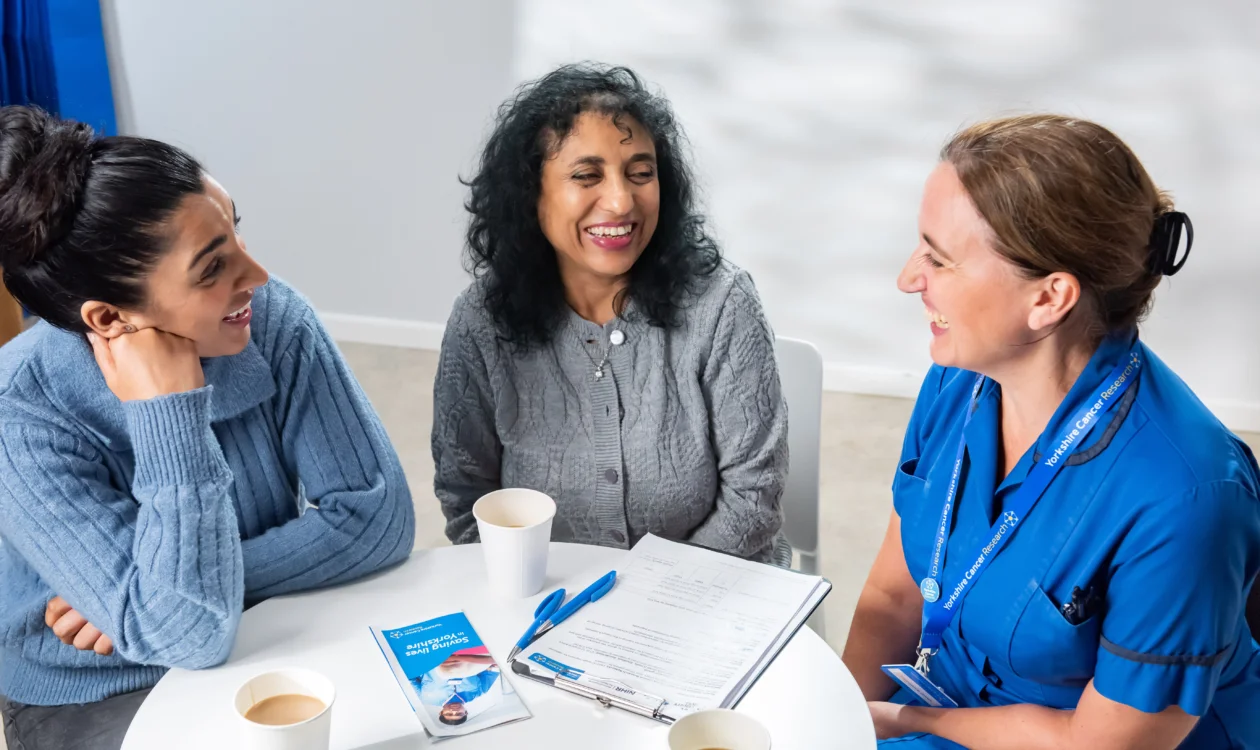 Two women and a female healthcare professional sit at a table chatting