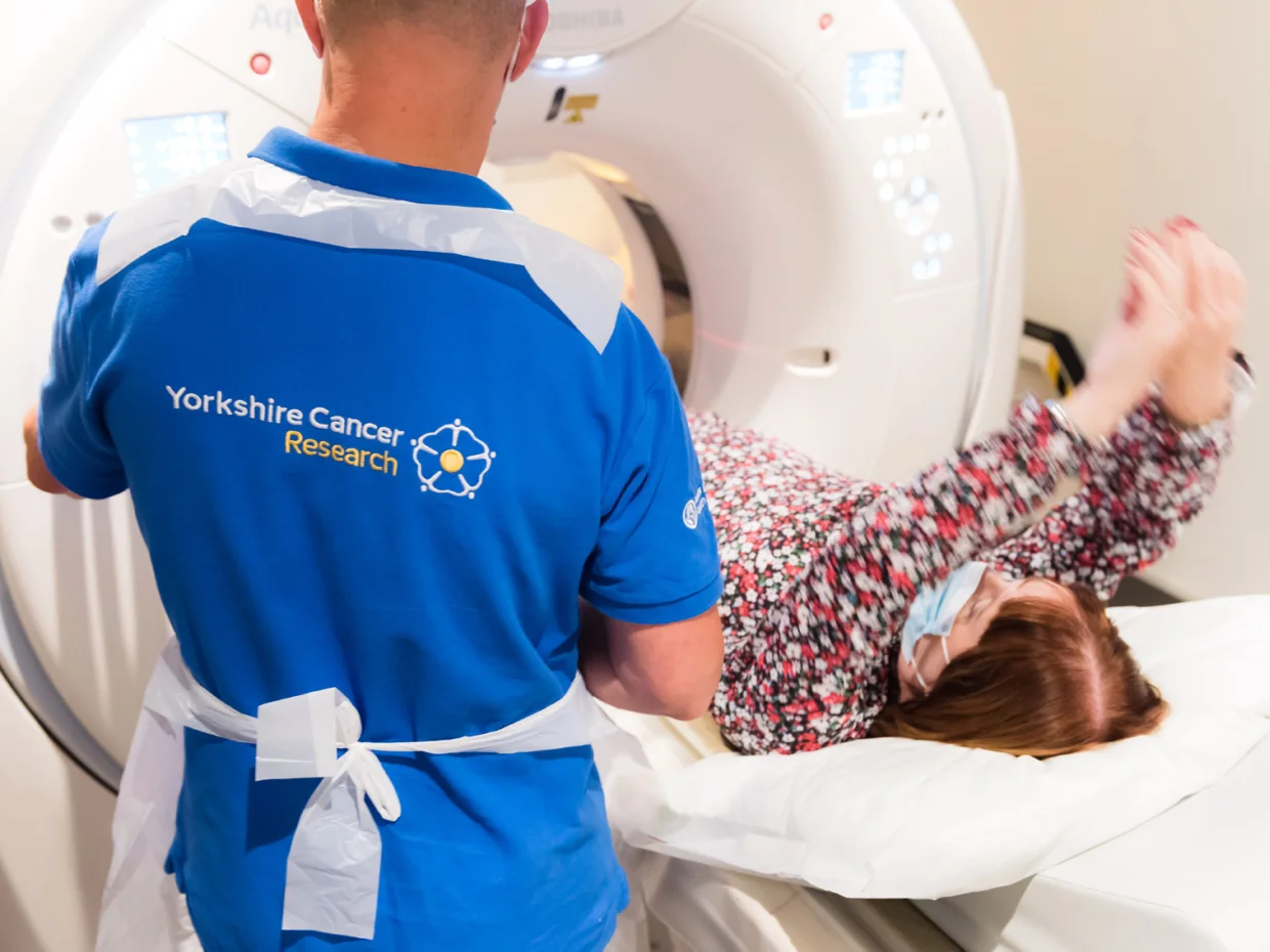 A woman is about to receive a CT scan. A scanning technician stands near to the scanner.