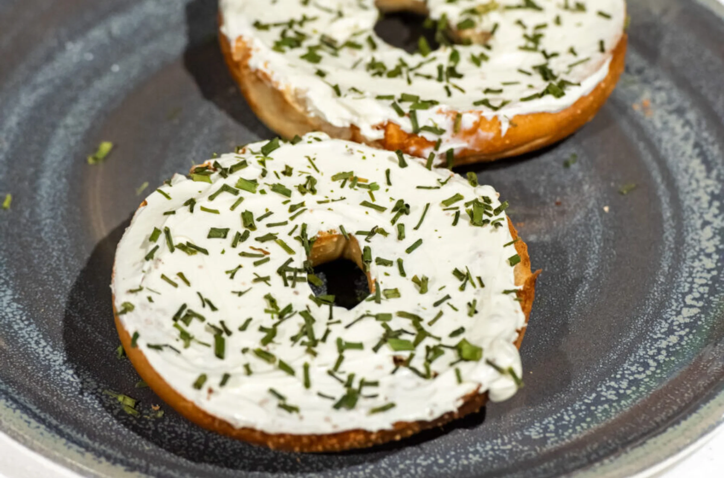 Two halves of a cream cheese and chive bagels on a blue speckled plate in the cafe