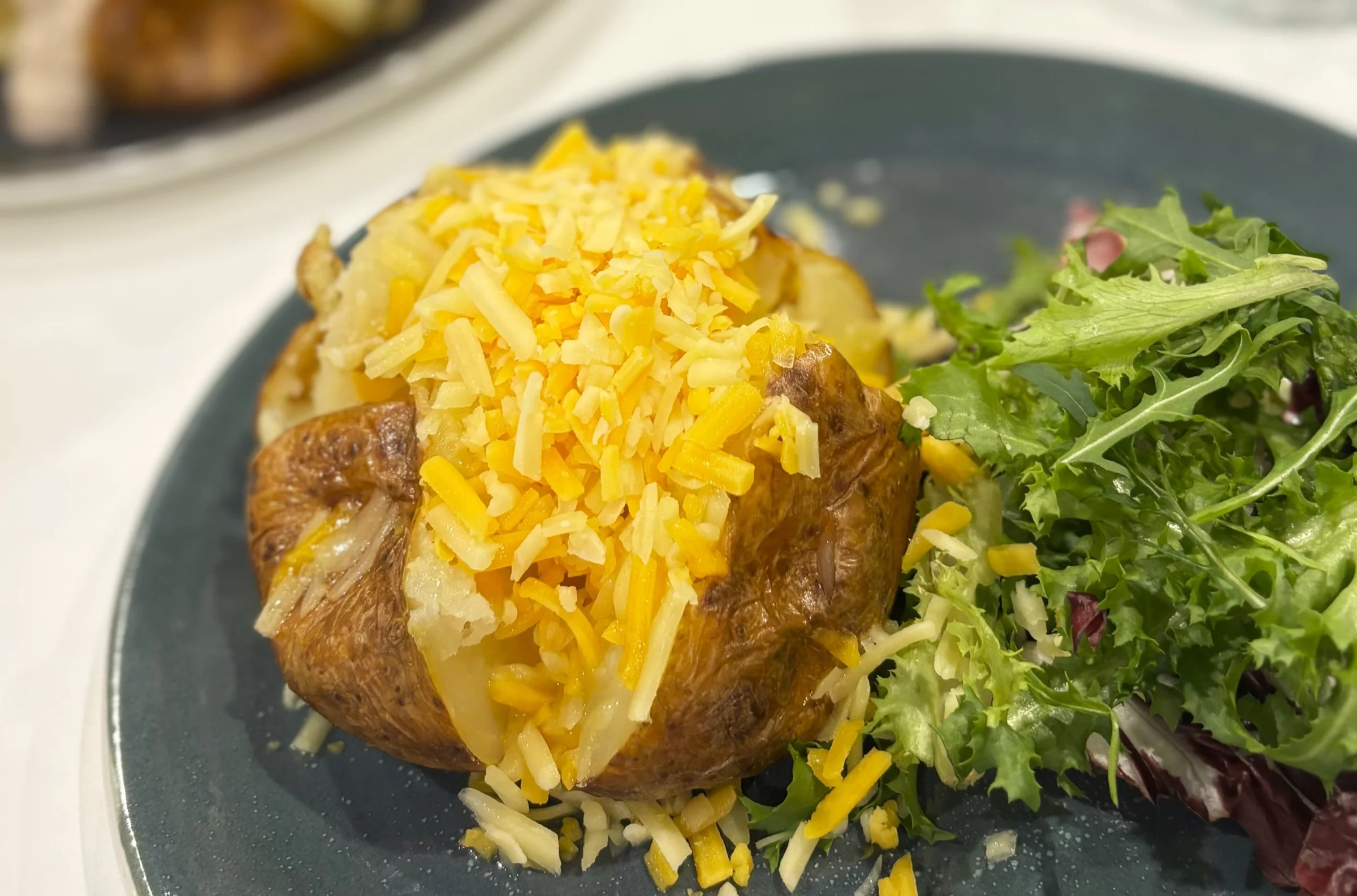 A cheesy jacket potato with a side salad sits on a blue plate in the cafe