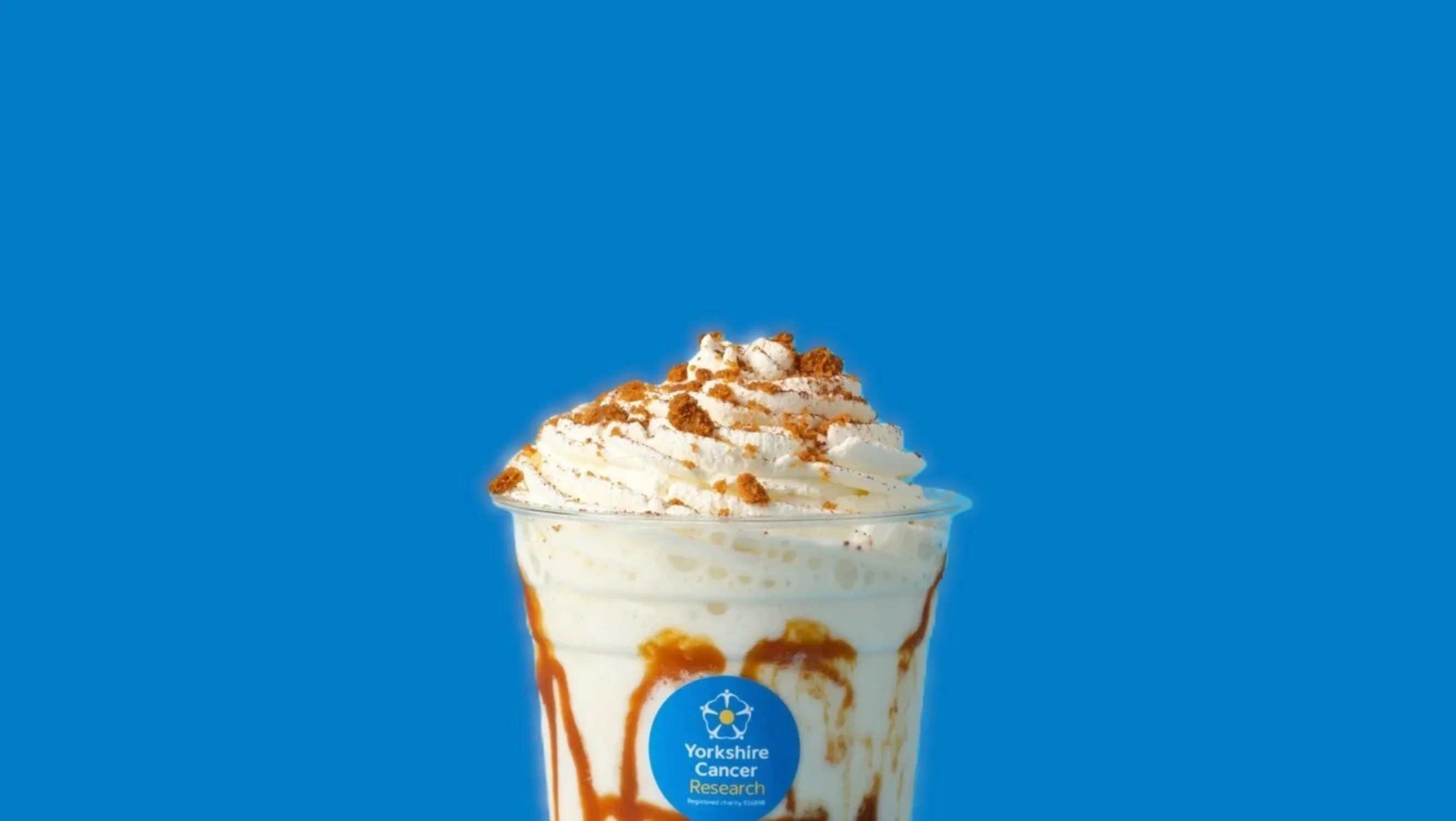 The top half of a banoffee pie smoothie with a Yorkshire Cancer Research sticker on the clear plastic cup. The milkshake has a dusting of biscuits on the top