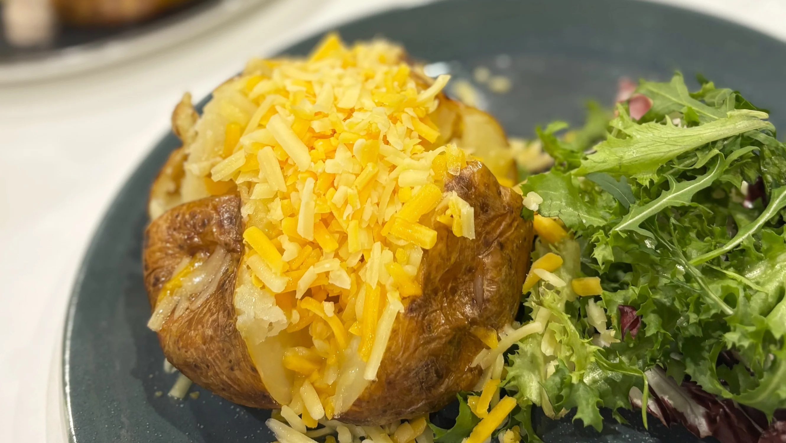 A cheesy jacket potato with a side salad sits on a blue plate in the cafe