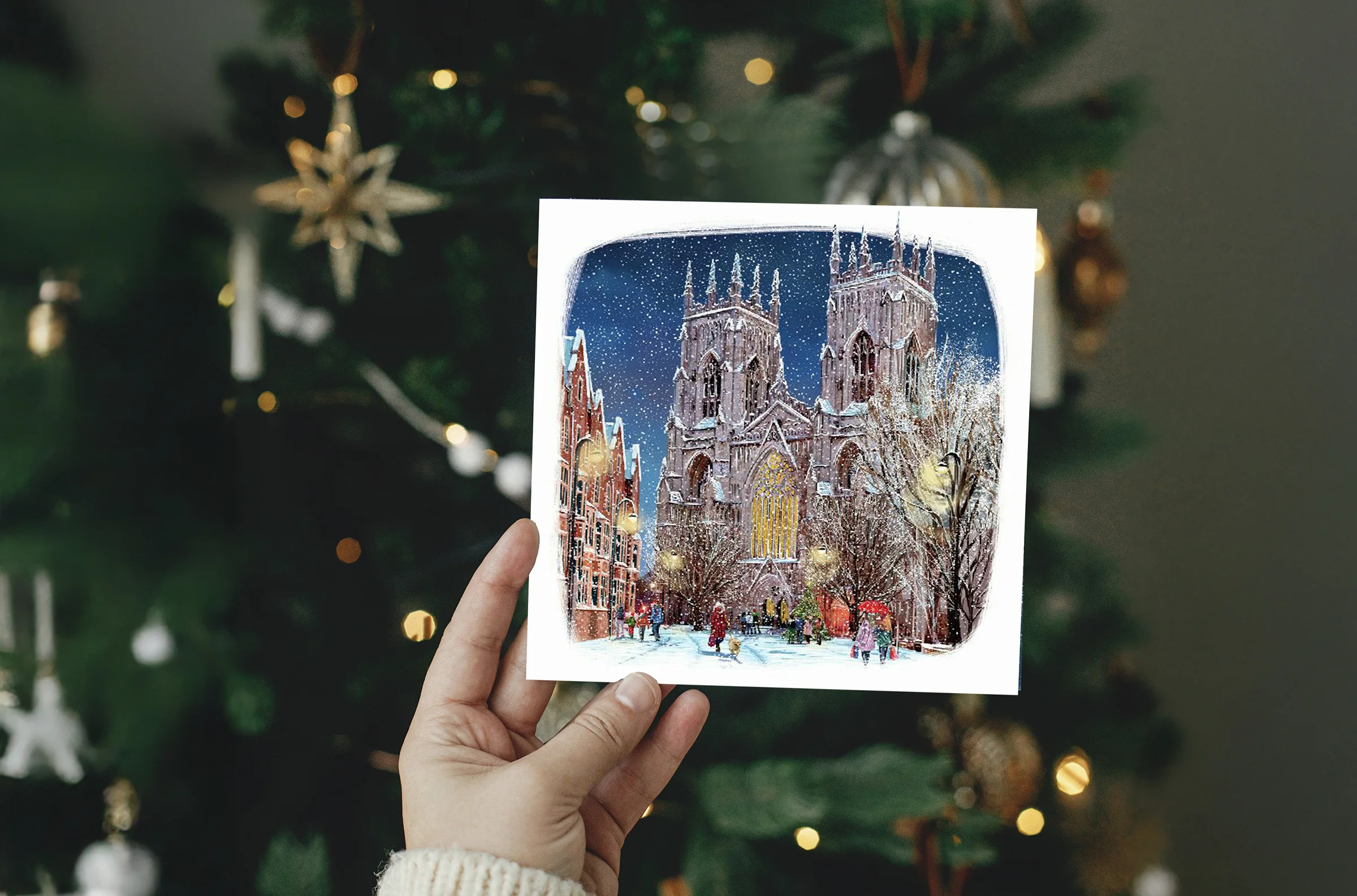 Christmas card featuring an illustration of York Minster, being held up by a hand in front of a decorated Christmas tree