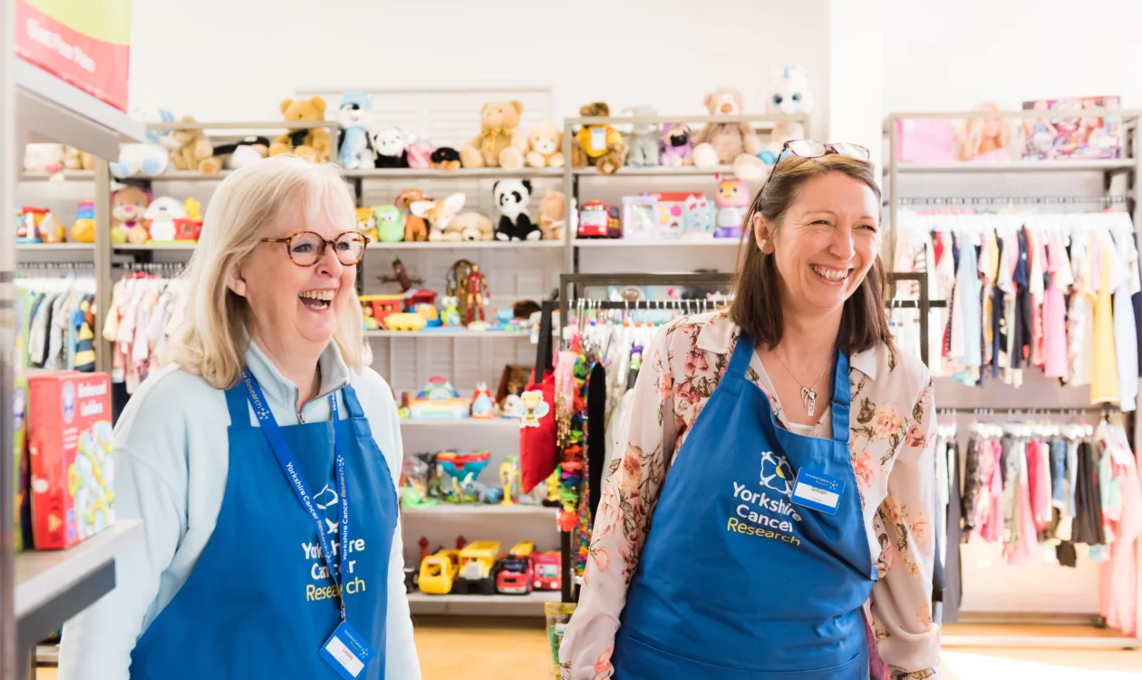 Volunteers inside a Yorkshire Cancer Research charity shop laughing and smiling