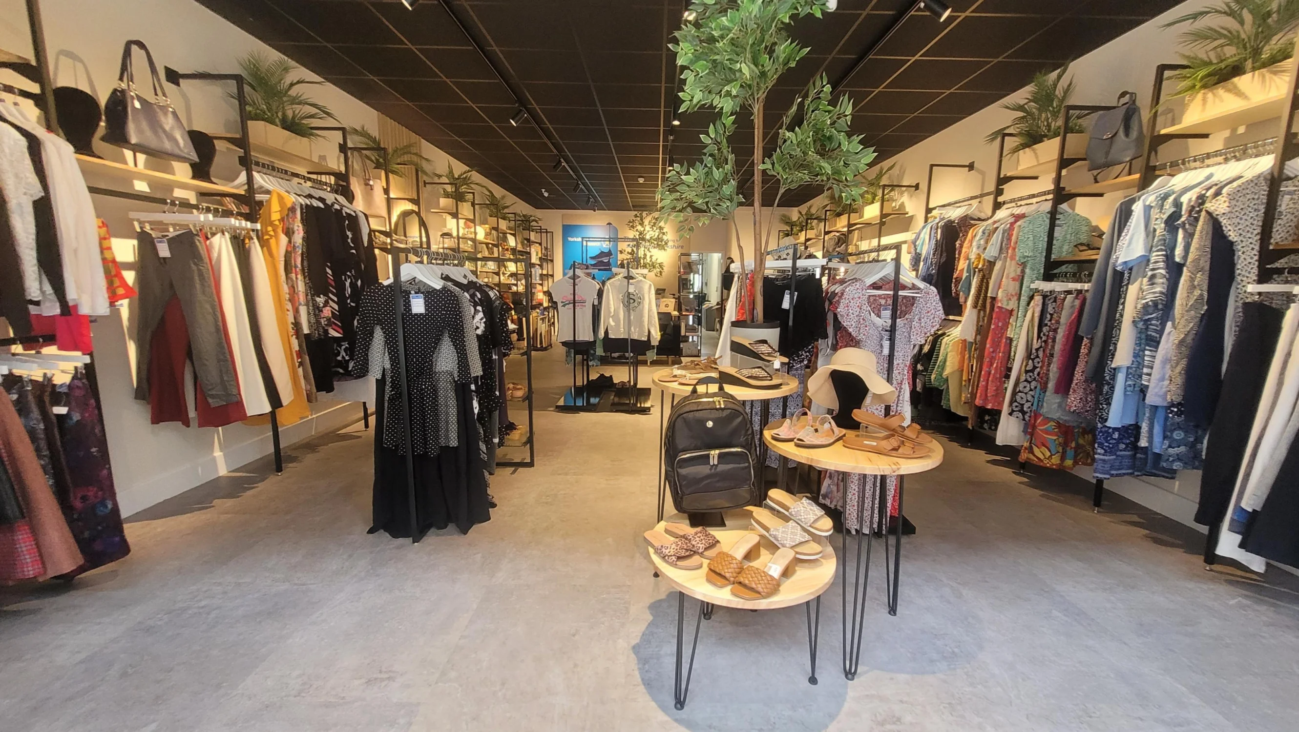 Inside of a modern shop looking from front to the back at a nice display of clothing, shoes, accessories