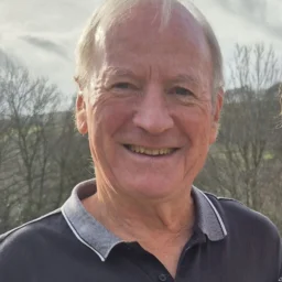 A man in a polo shirt smiles outside