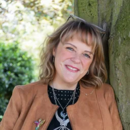 A lady leaning on a tree smiles at camera