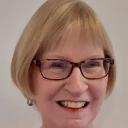 A lady with a blond bob and glasses smiles