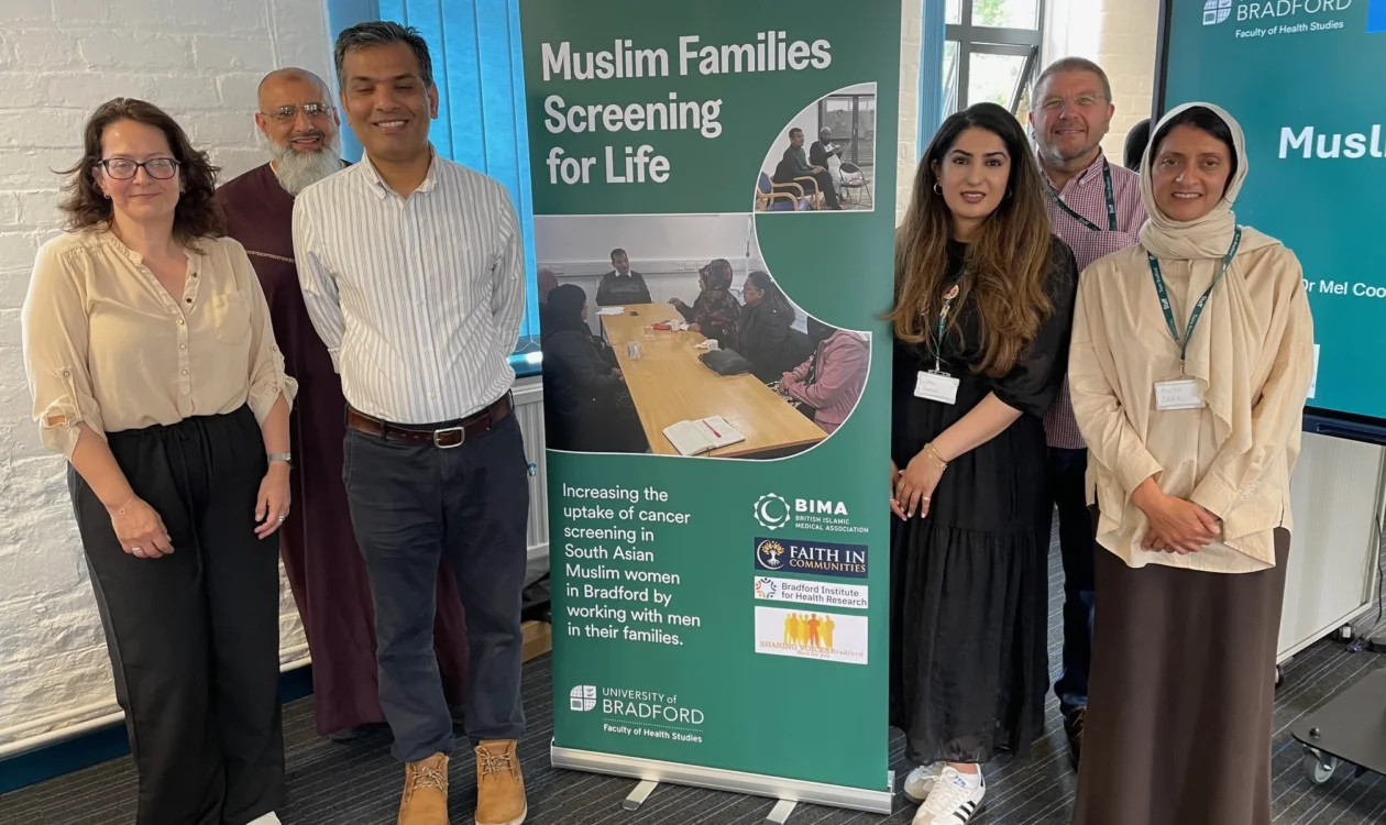 Researchers standing around a green pull-up banner with the words 'Muslime Families Screening For Life' printed.