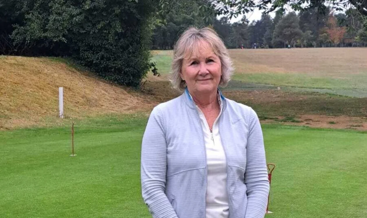 Anne with short hair standing on a golf court in a light blue jacket.