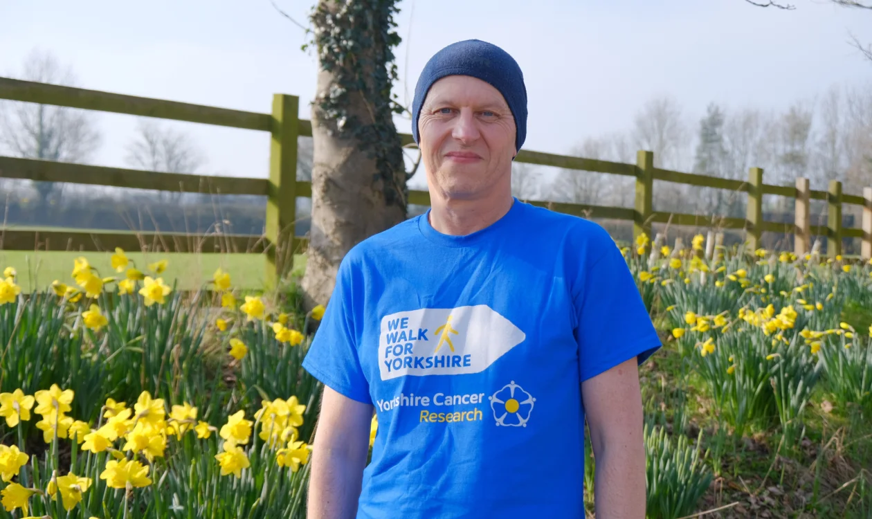 Simon Twigge standing and smiling at the camera in front of daffodils
