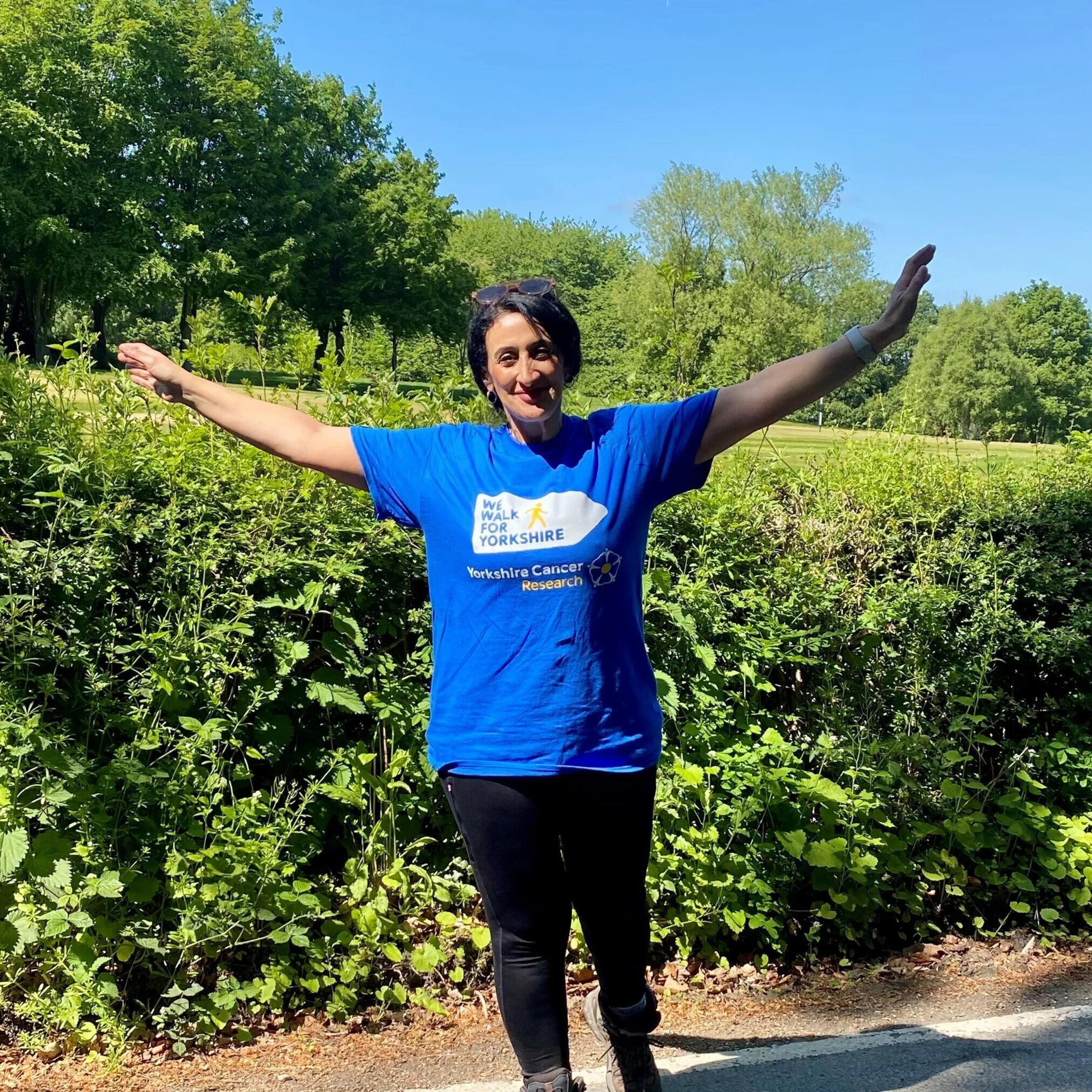 Professor Munitta Muthana with her hands in the air against the blue sky