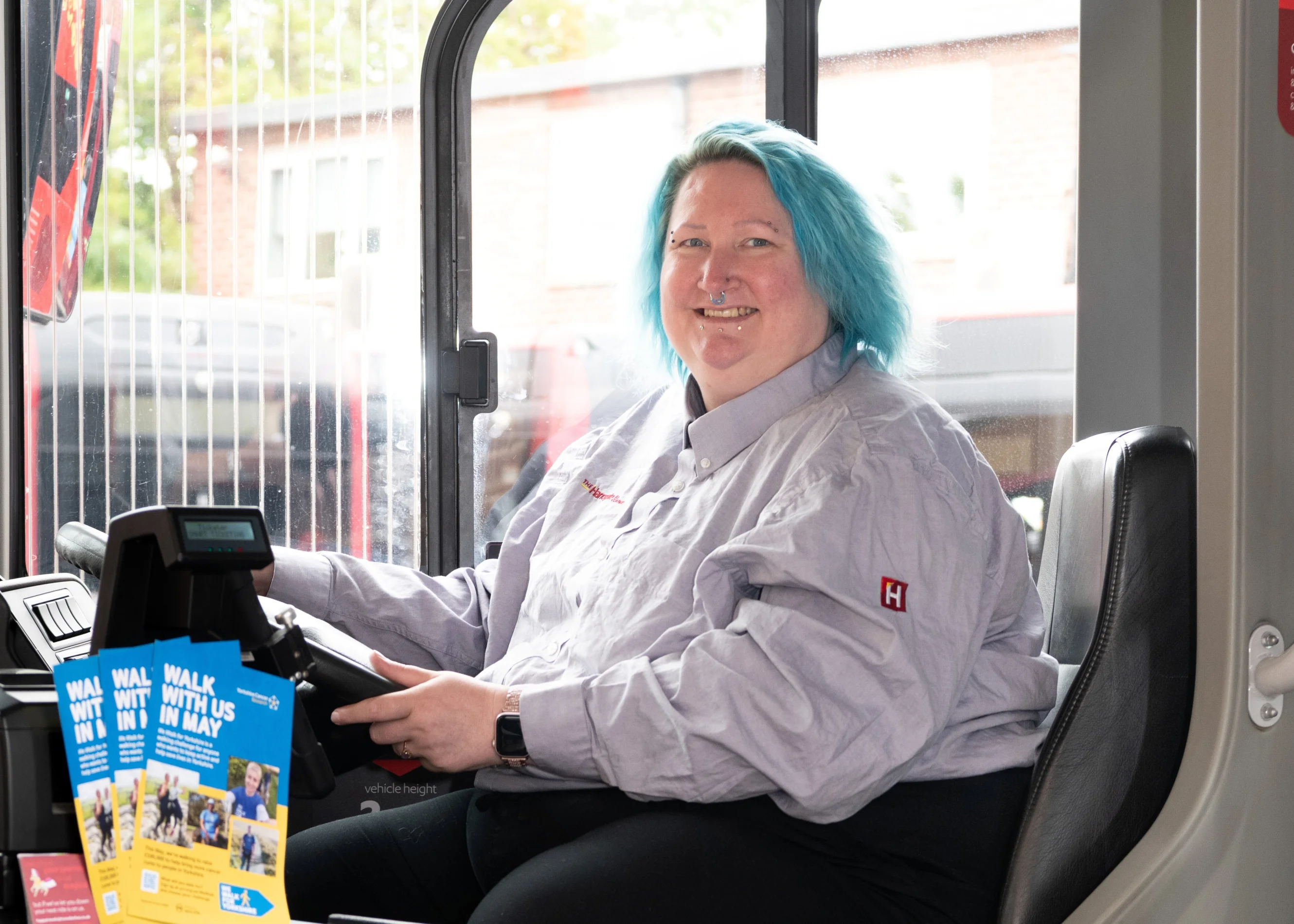 Sarah is wearing her uniform and sitting in the bus driver seat.