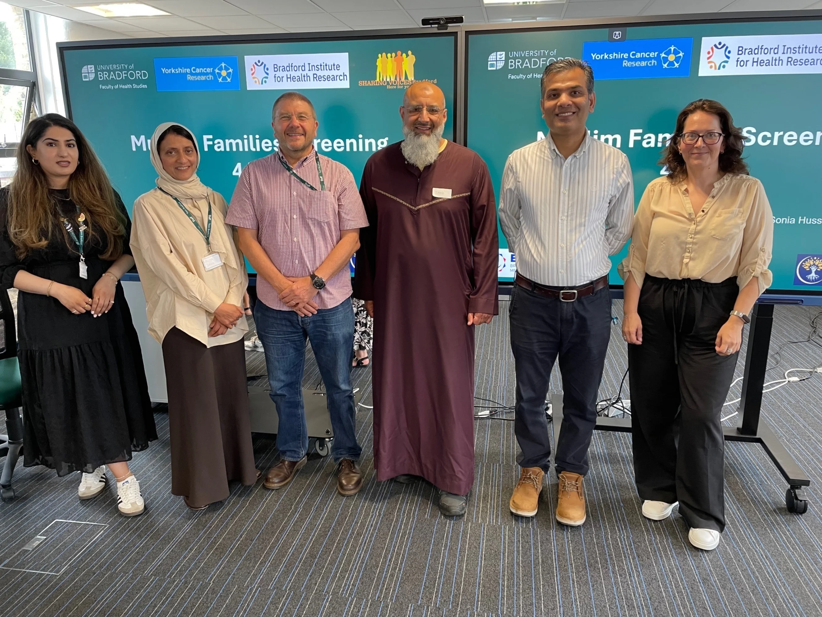 Researchers standing in front of two screens displaying text and the logos of the University of Bradford and Yorkshire Cancer Research.