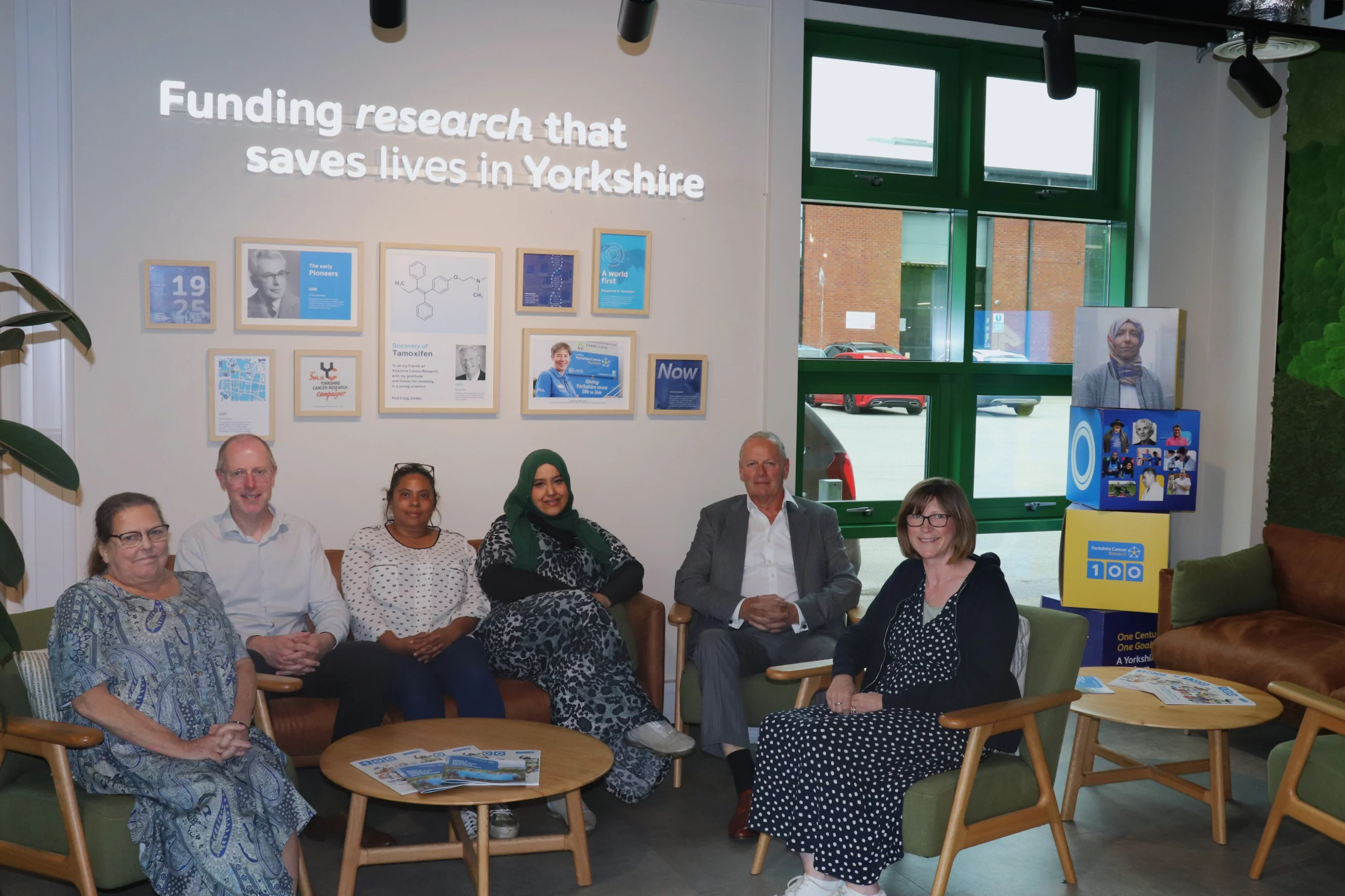 Members of the Research Advisory Panel sit around the Yorkshire Cancer Research Centre foyer, with a sign that says 'Funding research that save lives in Yorkshire'