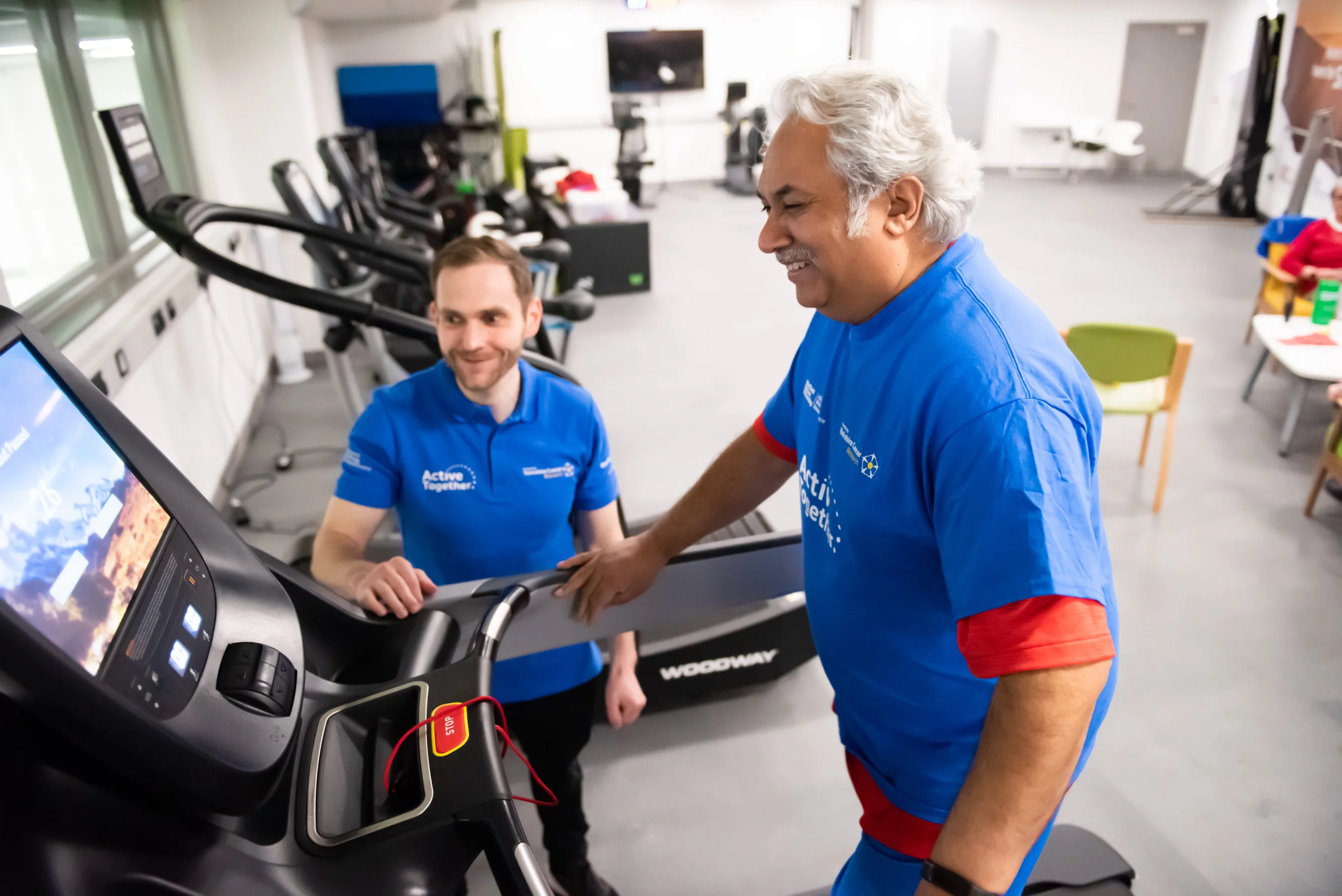 A middle aged man walking on a treadmill with a fitness instructor guiding him