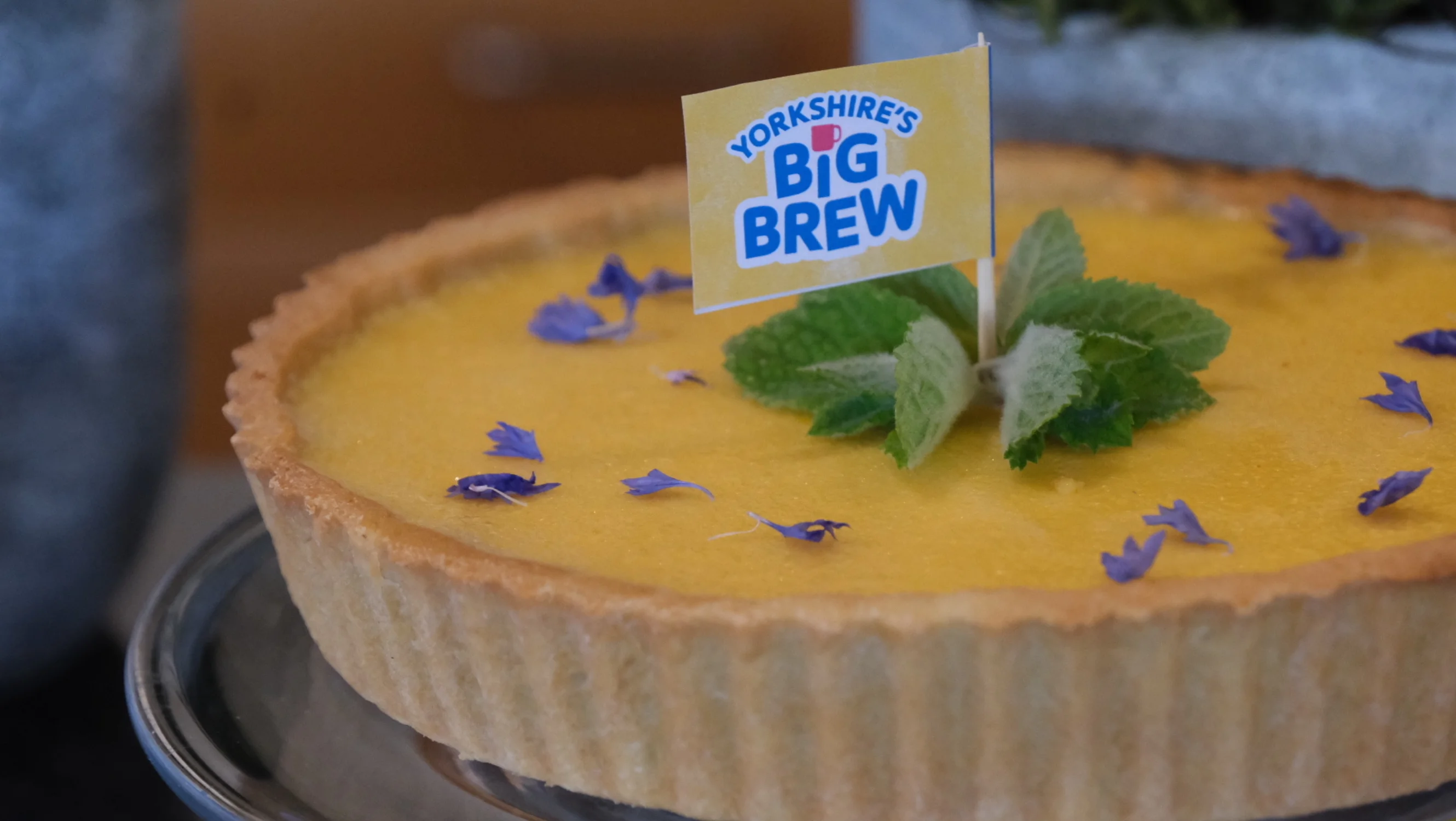 A close up of the lemon tart, featuring blue petals, mint leaves and a cake flag with the Yorkshire's Big Brew logo.