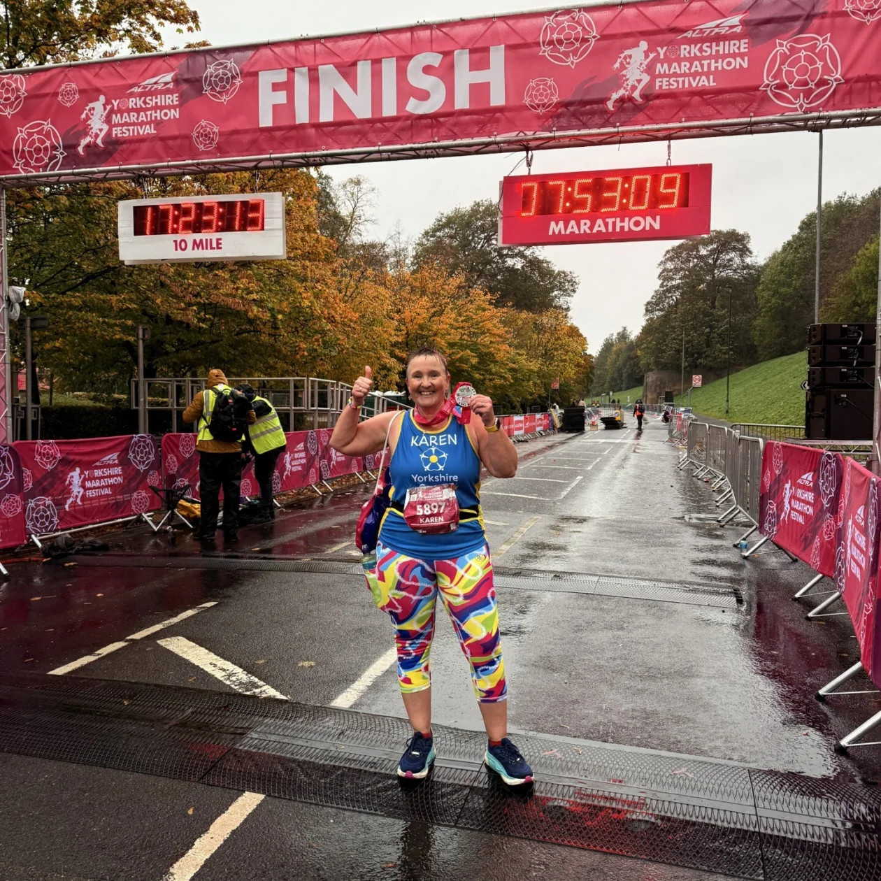 A lady stands at a finish line with a medal