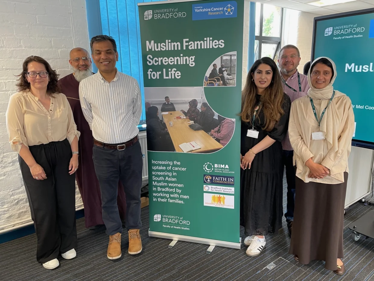 Researchers standing around a green pull-up banner with the words 'Muslime Families Screening For Life' printed.