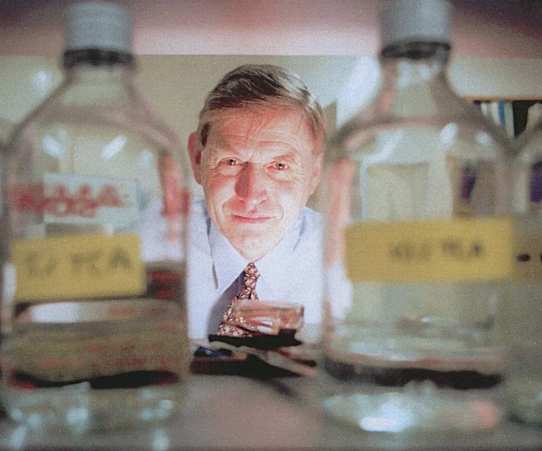 A man in shirt and tie stands in a lab pictured between glass bottles of solutions