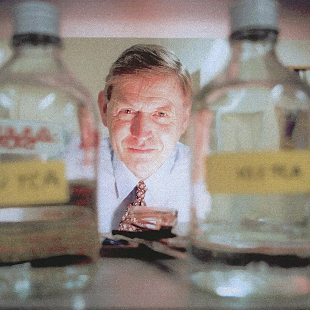 A man in shirt and tie stands in a lab pictured between glass bottles of solutions